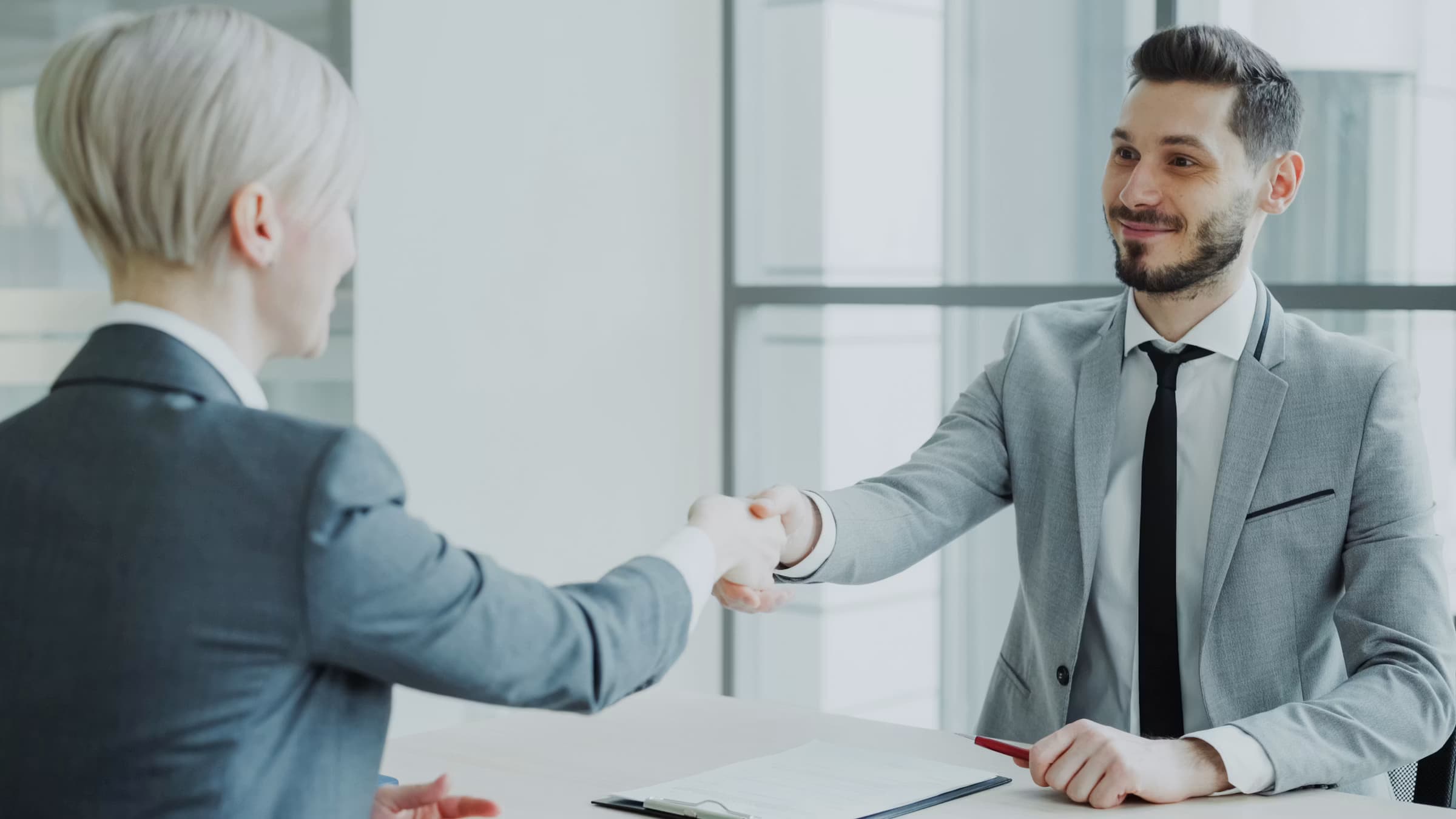 Two professionals shaking hands across a table in a modern office